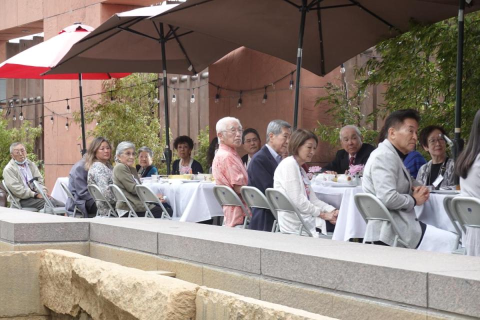 men and women have tea sitting at a long table listening to the speaker